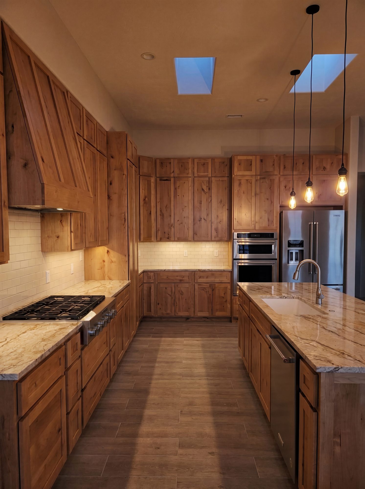 Rustic knotty alder kitchen at dusk with warm lighting, granite island and custom wood hood